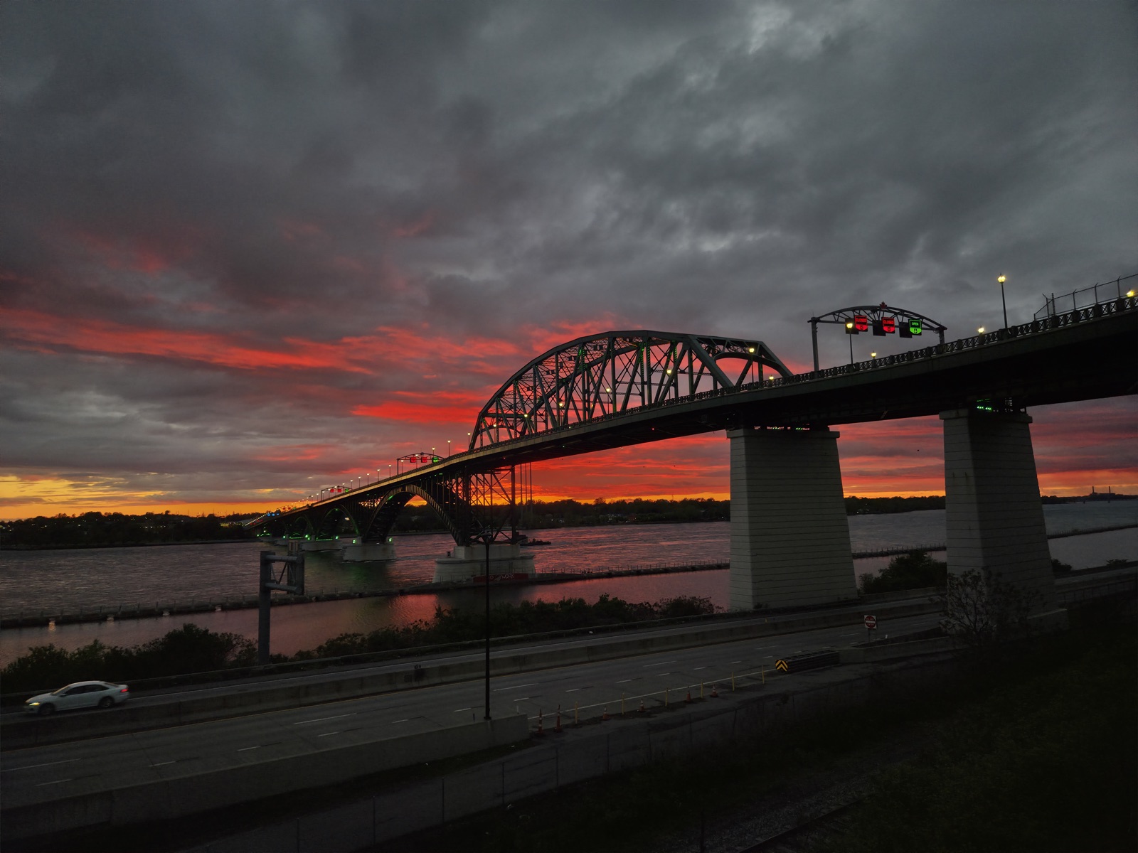 The Peace Bridge’s steel arch over the Niagara River against a red sunset, with the 190 in the foreground
